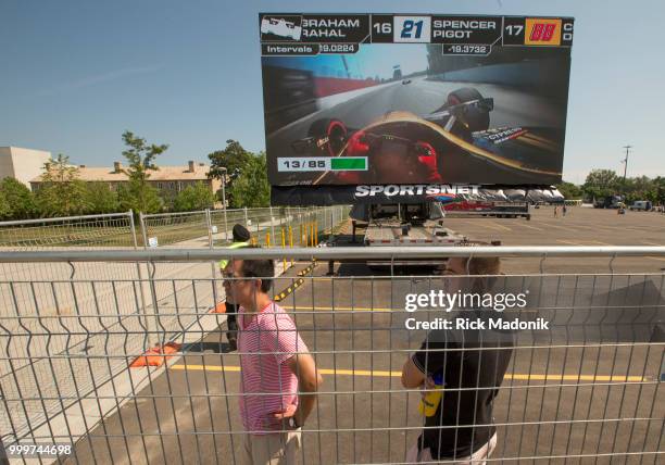 Spectators watch the action on the back straight away as a large screen gives a driver's view. Scott Dixon, of New Zealand, takes the checkered flag...