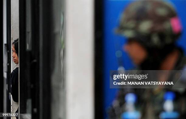 Thai woman hides behind a wall as a soldier takes position outside the Red Shirt anti-government protesters' camp in Bangkok on May 19, 2010. The...