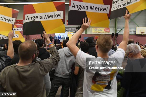Supporters hold up posters, Angela Merkel speaks in the background, during a CDU election campaign event in Wolgast, Germany, 08 September 2017....