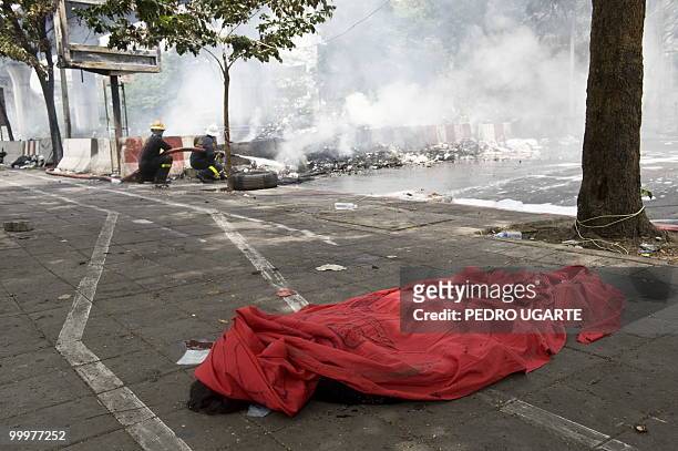 The body of a Red Shirt demonstrator lies on the floor wrapped in a red sheet as firemen douse the flames at a barricade during a Thai army crackdown...