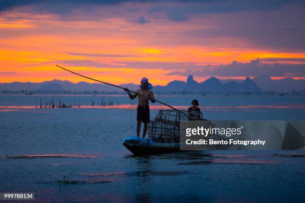 fisherman throw his net to catch to fish on the boat in twilight time - songkhla province stock pictures, royalty-free photos & images