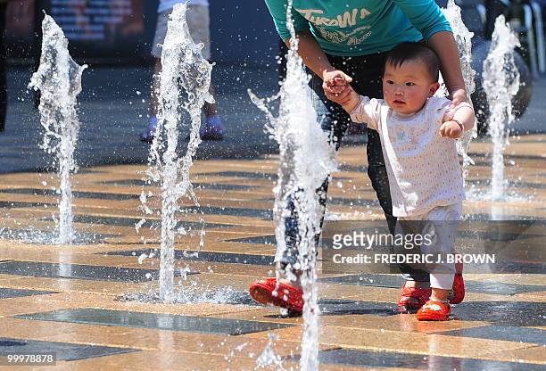 Child is assisted by an adult walking through a water fountain at a shopping mall in Beijing on May 19, 2010. China's rising economic prowess means...