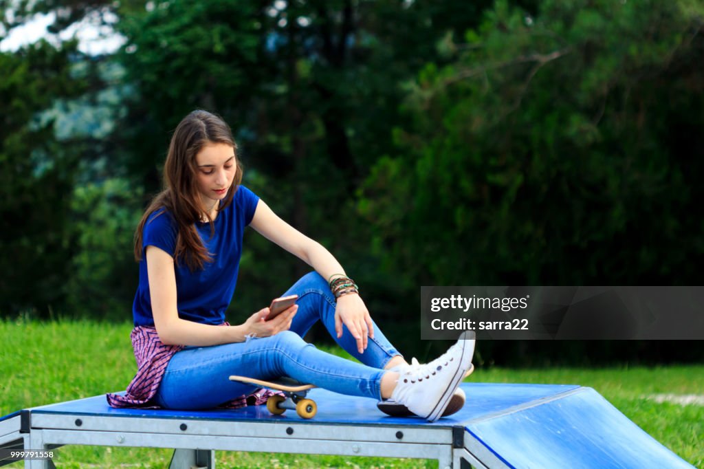 Beautiful teenage girl skater using phone