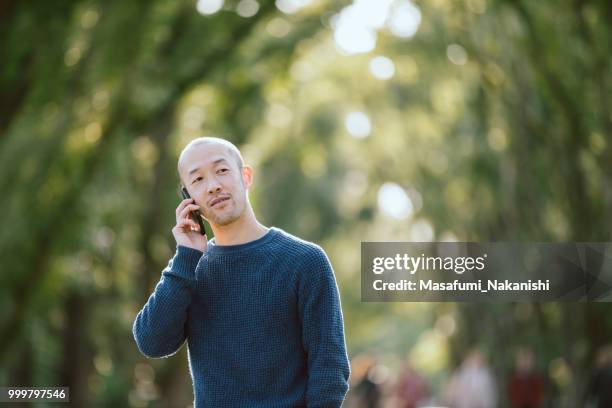 retratos de hombres asiáticos cabeza piel que con el smartphone en el parque - masafumi nakanishi fotografías e imágenes de stock