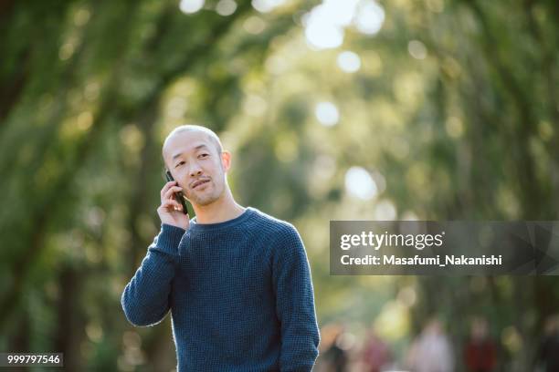portrait of skin head asian men calling with smartphone in the park - masafumi nakanishi imagens e fotografias de stock