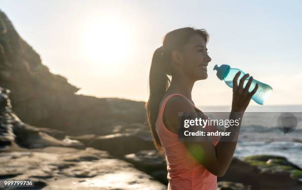 athletic woman at the beach drinking water - andresr stock pictures, royalty-free photos & images