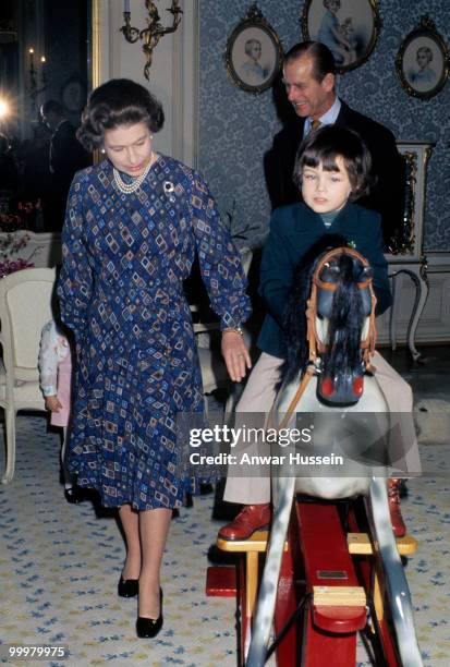 Queen Elizabeth ll and Prince Philip, Duke of Edinburgh play with a child riding a rocking horse in November 1976 in Luxembourg.
