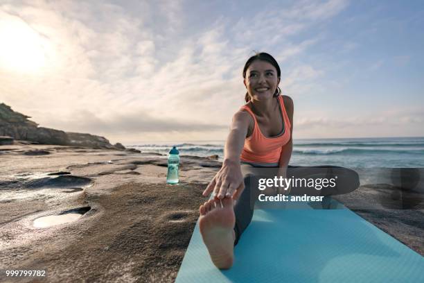 healthy woman doing yoga by the sea and stretching her legs - andresr stock pictures, royalty-free photos & images