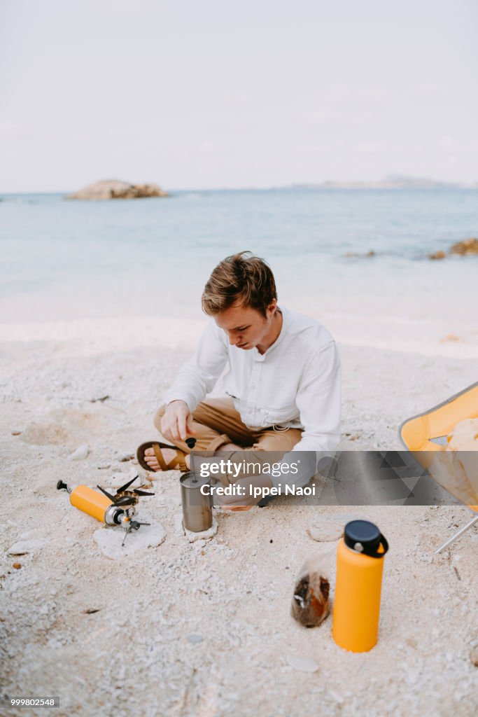 Man making coffee on tropical beach in morning while camping, Okinawa, Japan