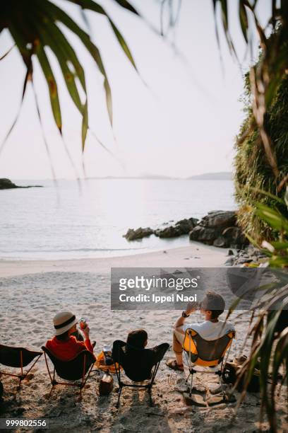 family sitting on camping chair on beach and enjoying sunset with beer, okinawa - ippei naoi fotografías e imágenes de stock