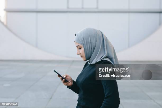 portrait of muslim woman texting with her smartphone. - iranian people stock pictures, royalty-free photos & images