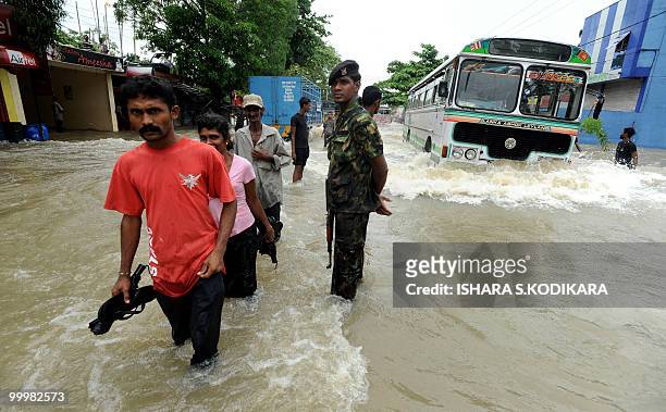 Sri Lankan residents are watched by a soldier as they walk through floodwaters in Seeduwa a suburb of Colombo on May 19, 2010. The military has been...
