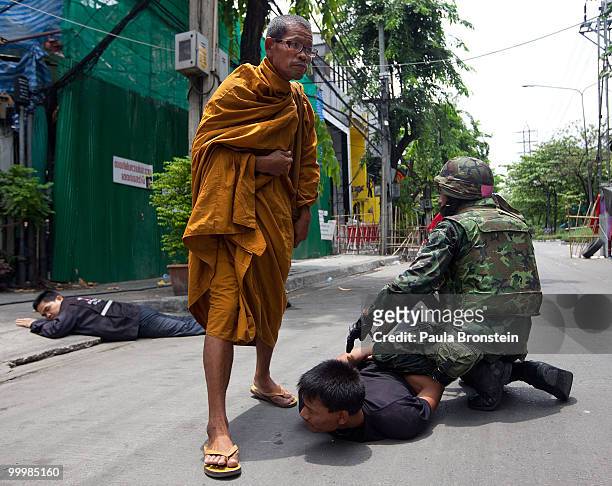 Monk watches as a red shirt anti-government protester surrenders to the military inside the red shirt camp on May 19, 2010 in Bangkok, Thailand. At...