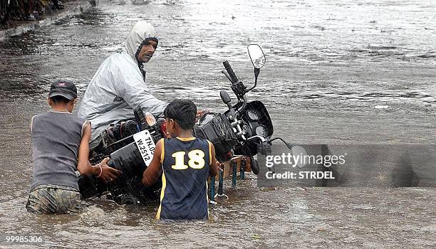 An Indian motorcyclist is assisted by youths as he uses a trolley to move his vehicle through floodwaters in Chennai on May 19 during heavy rain...