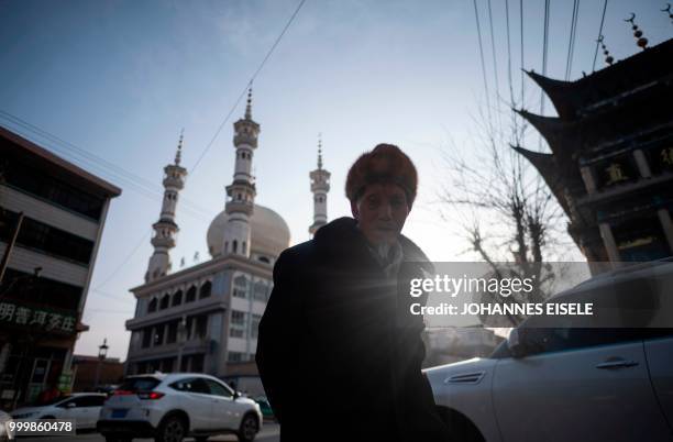 This picture taken on February 27, 2018 shows an ethnic Hui Muslim man walking before a mosque in Guanhe, China's Gansu province. - Green-domed...