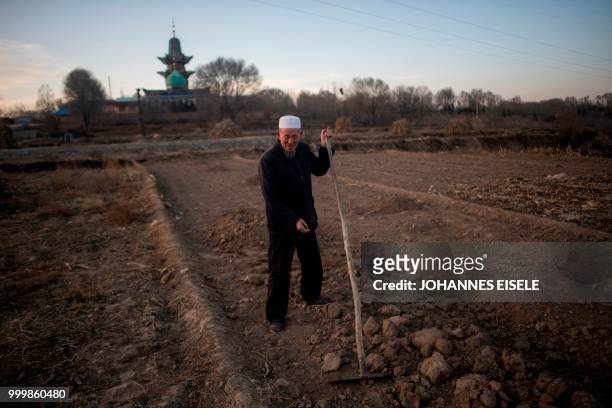 This picture taken on March 2, 2018 shows an ethnic Hui Muslim man working in his field in front of a mosque in the suburbs of Linxia, China's Gansu...