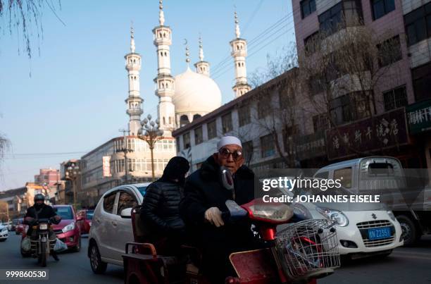 This picture taken on February 27, 2018 shows an ethnic Hui Muslim man commuting on a street before a mosque in Guanhe, China's Gansu province. -...