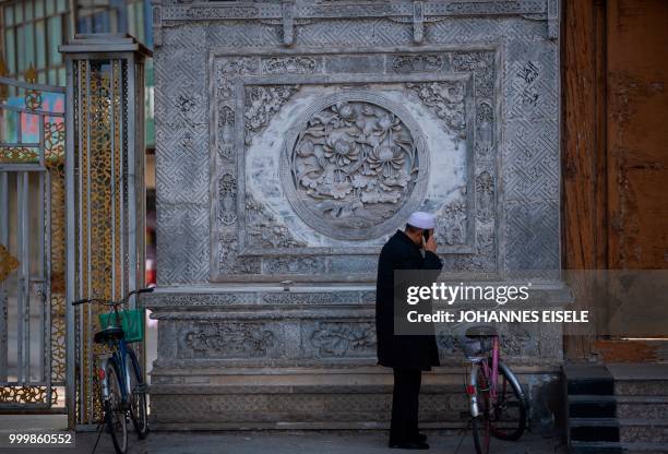 This picture taken on February 27, 2018 shows an ethnic Hui Muslim man using his mobile phone inside a courtyard of a mosque in Guanhe, China's Gansu...