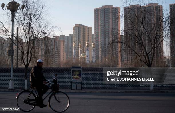 This picture taken on March 2, 2018 shows an ethnic Hui Muslim man riding past a mosque in Linxia, China's Gansu province. - Green-domed mosques...