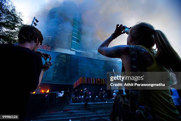 Tourists take photos of a fire burn at the Central World Shopping Mall on May 19, 2010 in Bangkok, Thailand. At least 5 people are reported to have...