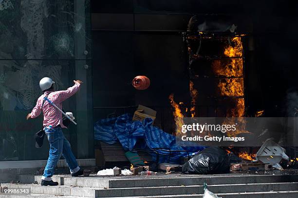 Thai anti-government red shirt protester throws a propane tank onto a fire set at the CentralWorld mall on May 19, 2010 in Bangkok, Thailand. At...