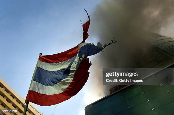 Battered Thai flag flaps in the wind as smoke rises from the CentralWorld mall on May 19, 2010 in Bangkok, Thailand. At least 5 people are reported...