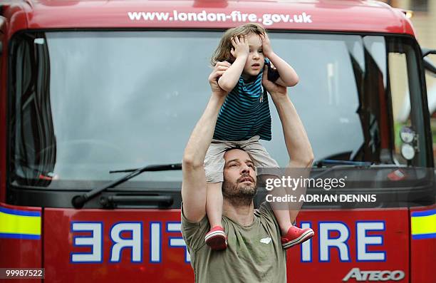 Man holds a child on his shoulders to watch firemen tackling a rooftop blaze on a roof above an apartment in London on May 19, 2010. The building was...