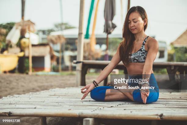 woman doing yoga meditation and stretching exercises at the beach - south_agency stock pictures, royalty-free photos & images