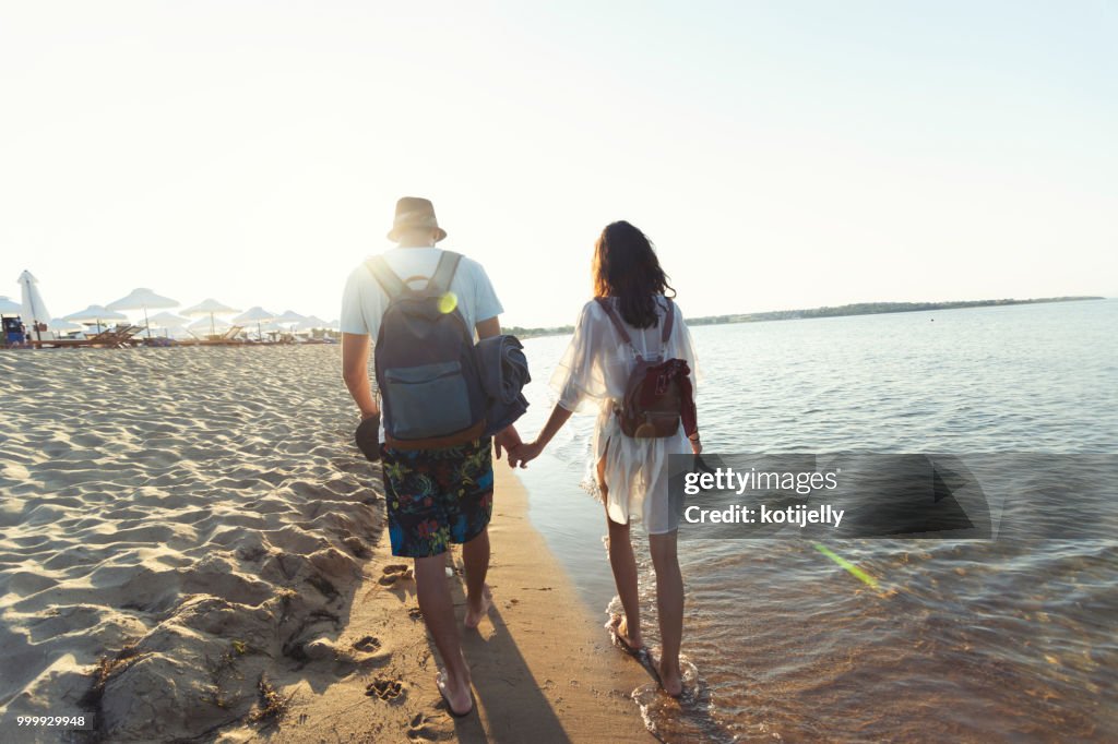 Two young people holding hands and walking on beach