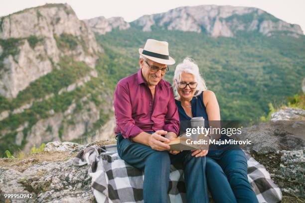 loving senior couple hiking, sitting on the top of rock, exploring. active mature man and woman hugging and happily smiling. - woman sitting top man stock pictures, royalty-free photos & images