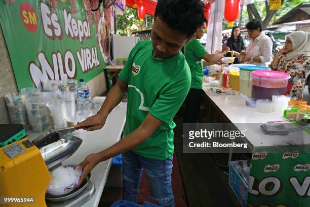 An employee crushes ice while preparing an order of Milo on round ice snack at an Es Kepal Milo Viral street stall in the Tebet area of Jakarta,...