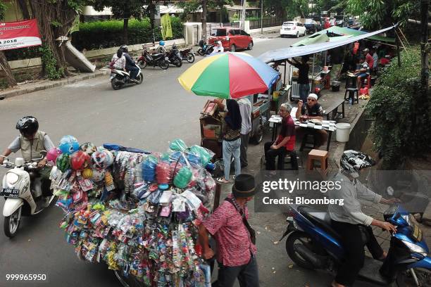 Toy vendor pulls his cart past street food stalls in the Tebet area of Jakarta, Indonesia, on Friday, July 13, 2018. Cocoa production in the 130-year...