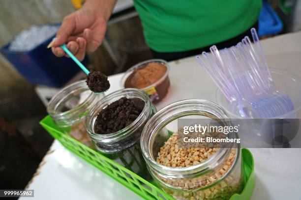 An employee scoops a spoonful of brown sugar while preparing an order of Milo on round ice snack at an Es Kepal Milo Viral street stall in the Tebet...