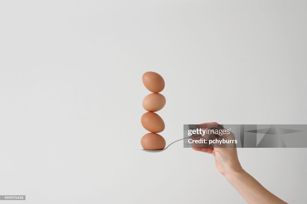 Woman's hand holding a spoon with four eggs balancing on top of each other