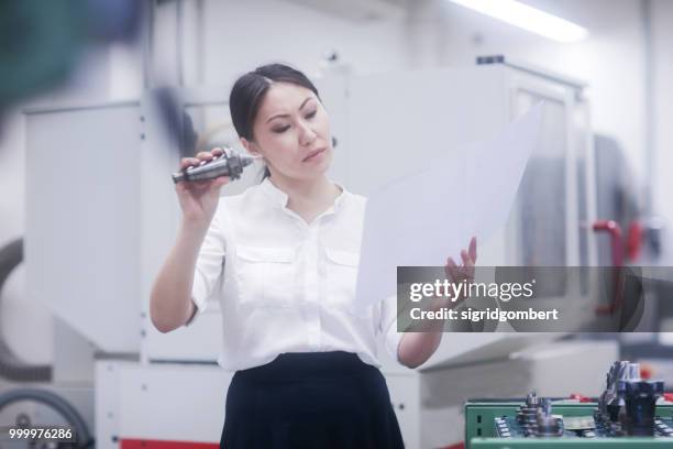 female engineer looking at a technical drawing and examining a drill bit - drill bit stockfoto's en -beelden