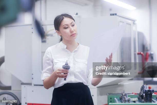 female engineer looking at a technical drawing and examining a drill bit - drill bit - fotografias e filmes do acervo