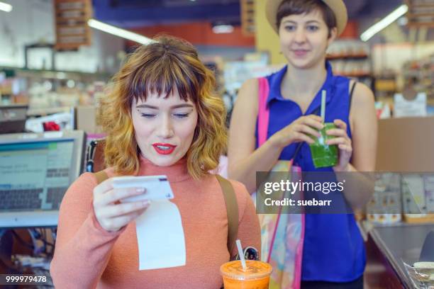 two women in a shop paying for fresh juice drinks - beleg stock-fotos und bilder