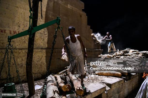 In this photograph taken on June 2, 2018 members of the Dom community use a scale to weigh wood that is used for cremations at the Manikarnika Ghat...