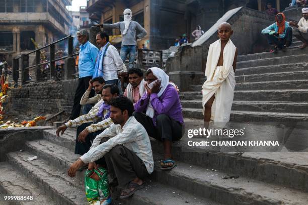 In this photograph taken on June 2, 2018 Indian men wait for a dead body to finish being cremated at the Manikarnika Ghat in the old quarters of...