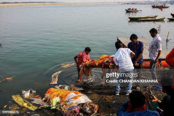 In this photograph taken on June 2, 2018 Indian men dip a dead body into the river Ganges prior to the cremation at the Manikarnika Ghat in the old...