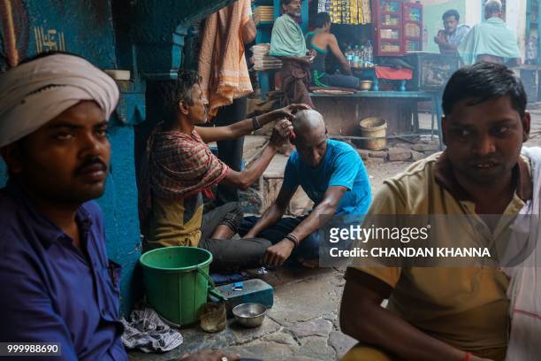 In this photograph taken on June 2, 2018 an Indian man gets his head shaved at the Manikarnika Ghat in the old quarters of Varanasi. - The Doms are a...