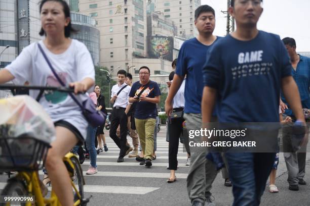 People cross a road in a commercial district in Beijing on July 16, 2018. - China said on July 16 its economic growth slowed slightly in the second...