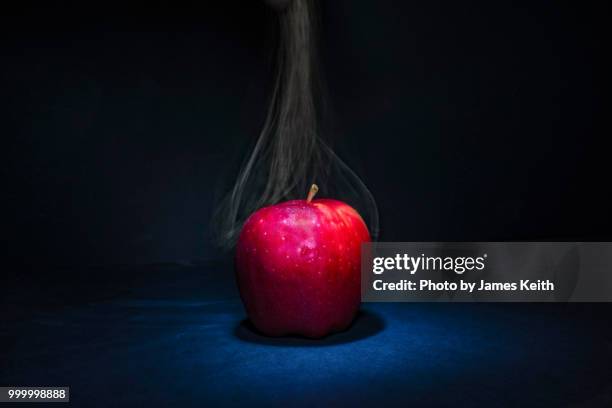 smoke appears to be emanating from a red apple in the spotlight. - james hale stock pictures, royalty-free photos & images