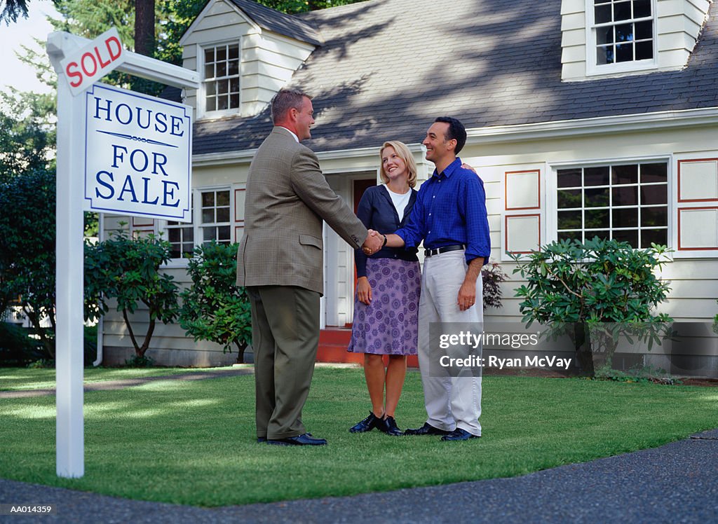 Real estate agent and couple standing in front of sold house