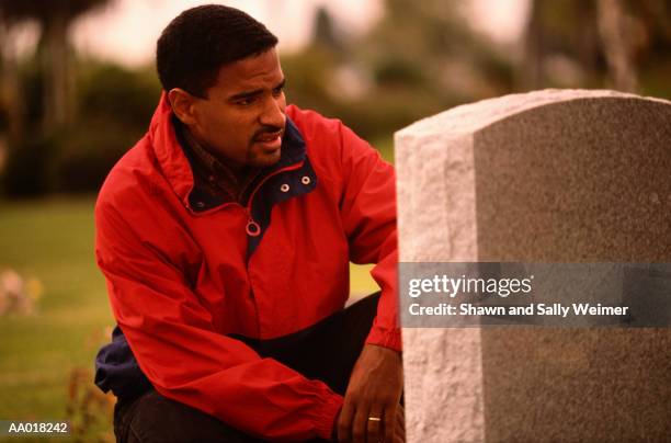 pensive man looking at a tombstone in a cemetery - widower stock pictures, royalty-free photos & images