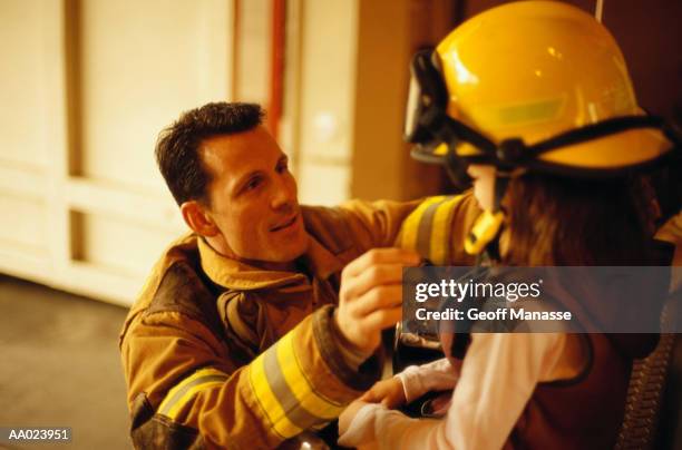 firefighter putting his helmet on a girl - firefighter getting dressed stock pictures, royalty-free photos & images