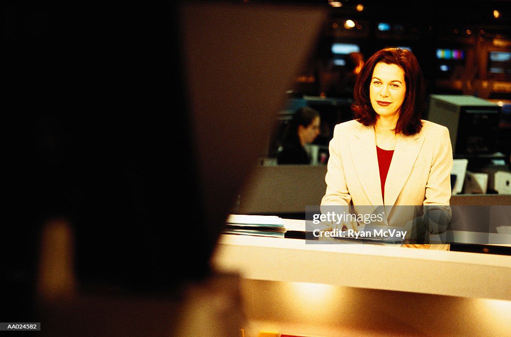 Television anchorwoman sitting at desk smiling at camera