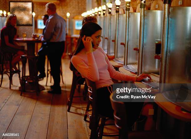 young woman on cellular phone in internet cafe - ciber café imagens e fotografias de stock