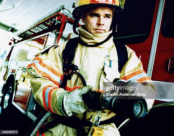 firefighter holding hose, standing in front of fire engine - emergency services equipment stock pictures, royalty-free photos & images