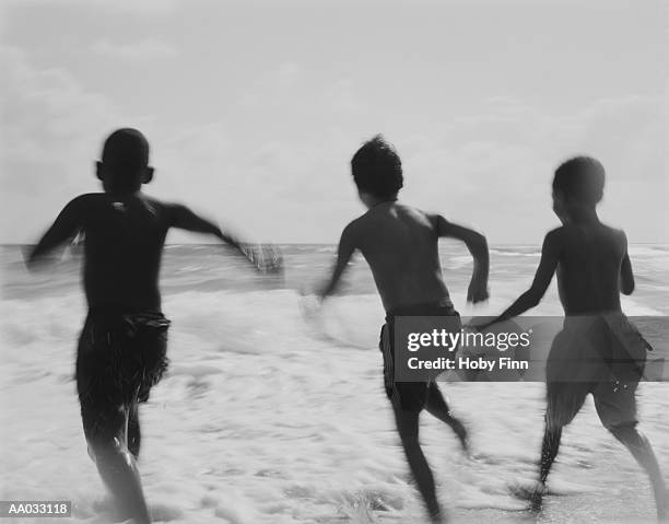 three young boys running into the ocean - street child stock pictures, royalty-free photos & images